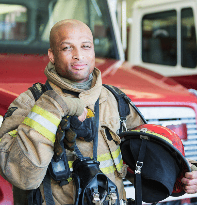 African American male firefighter standing in front of firetruck - Honoring Our Heroes program