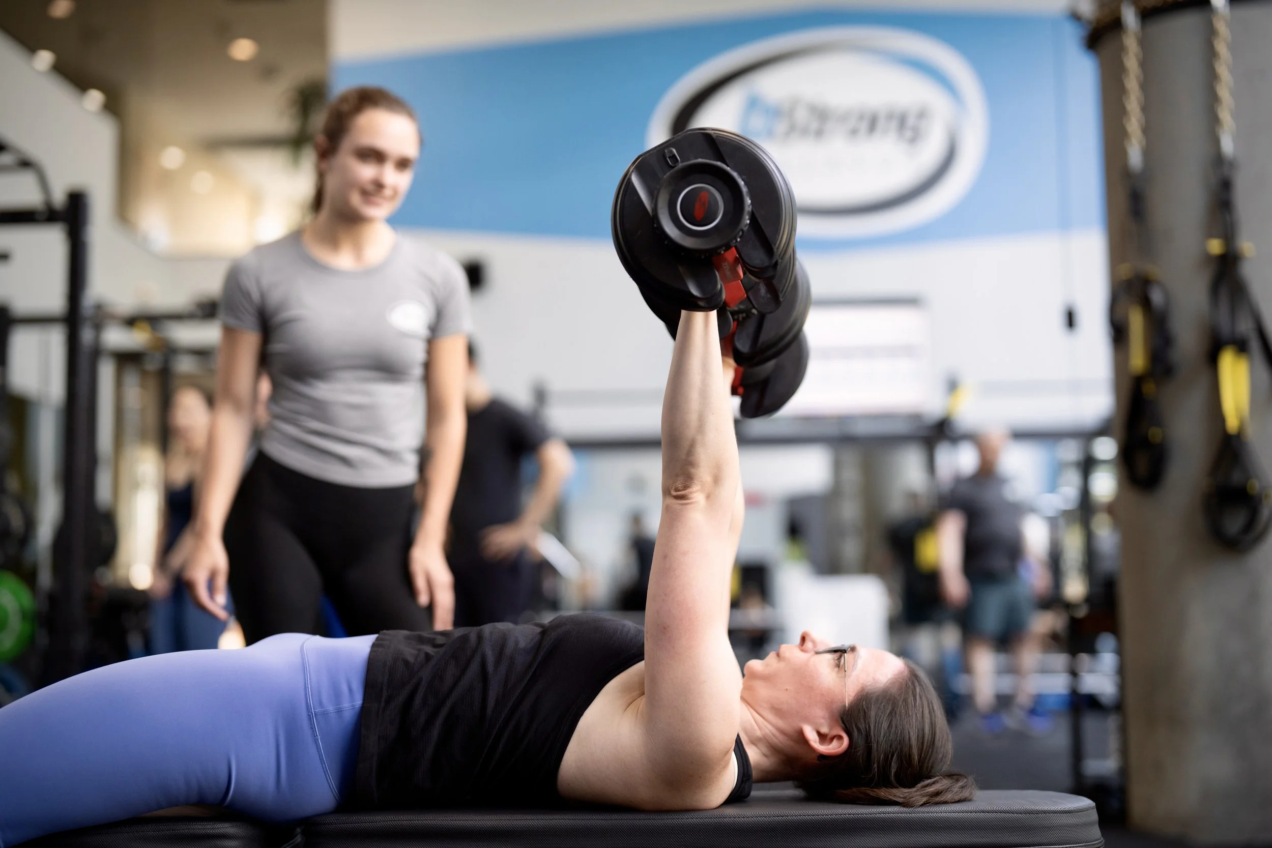 Member performing chest press with personal trainer watching closely