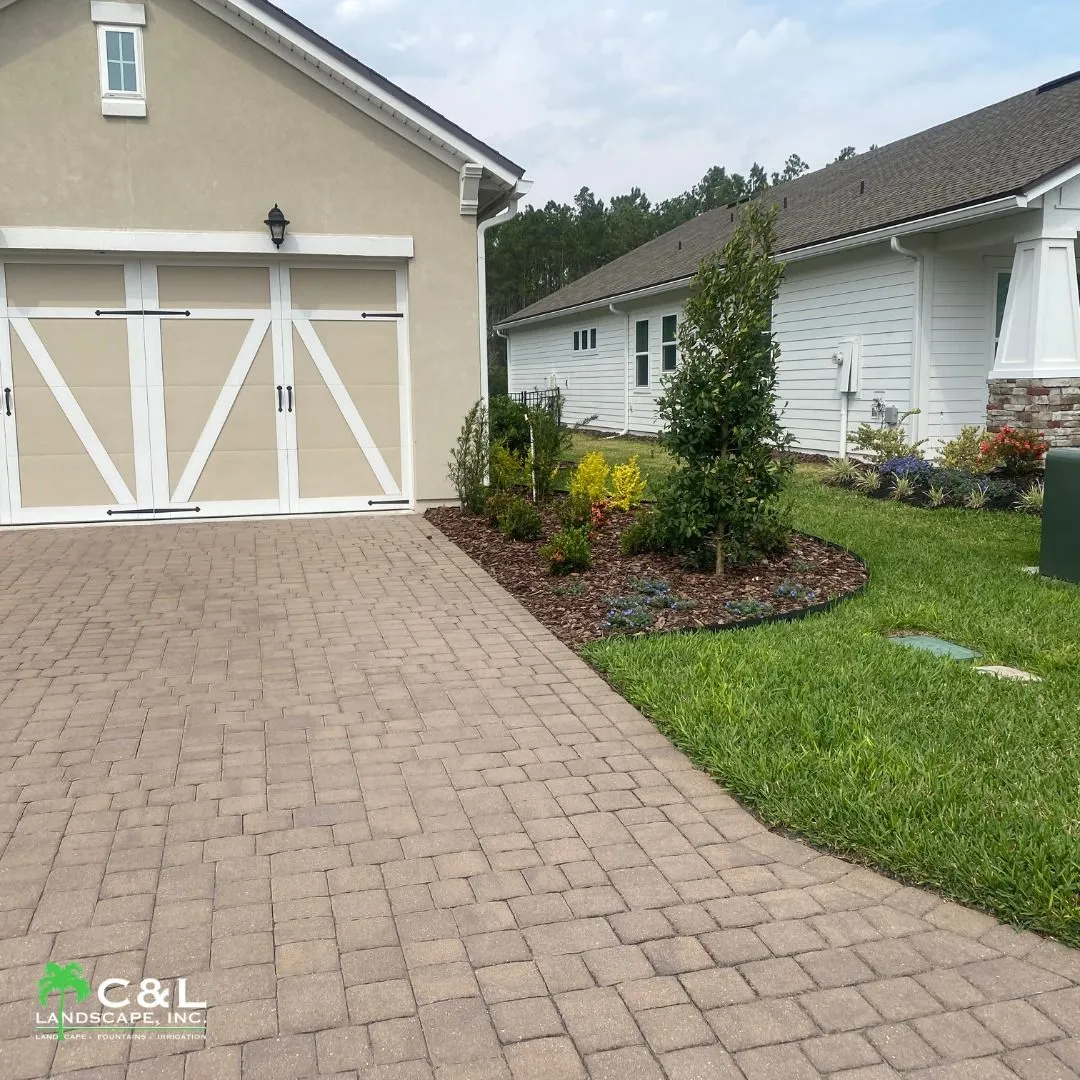 Brick driveway with planted landscaping and beautiful white house