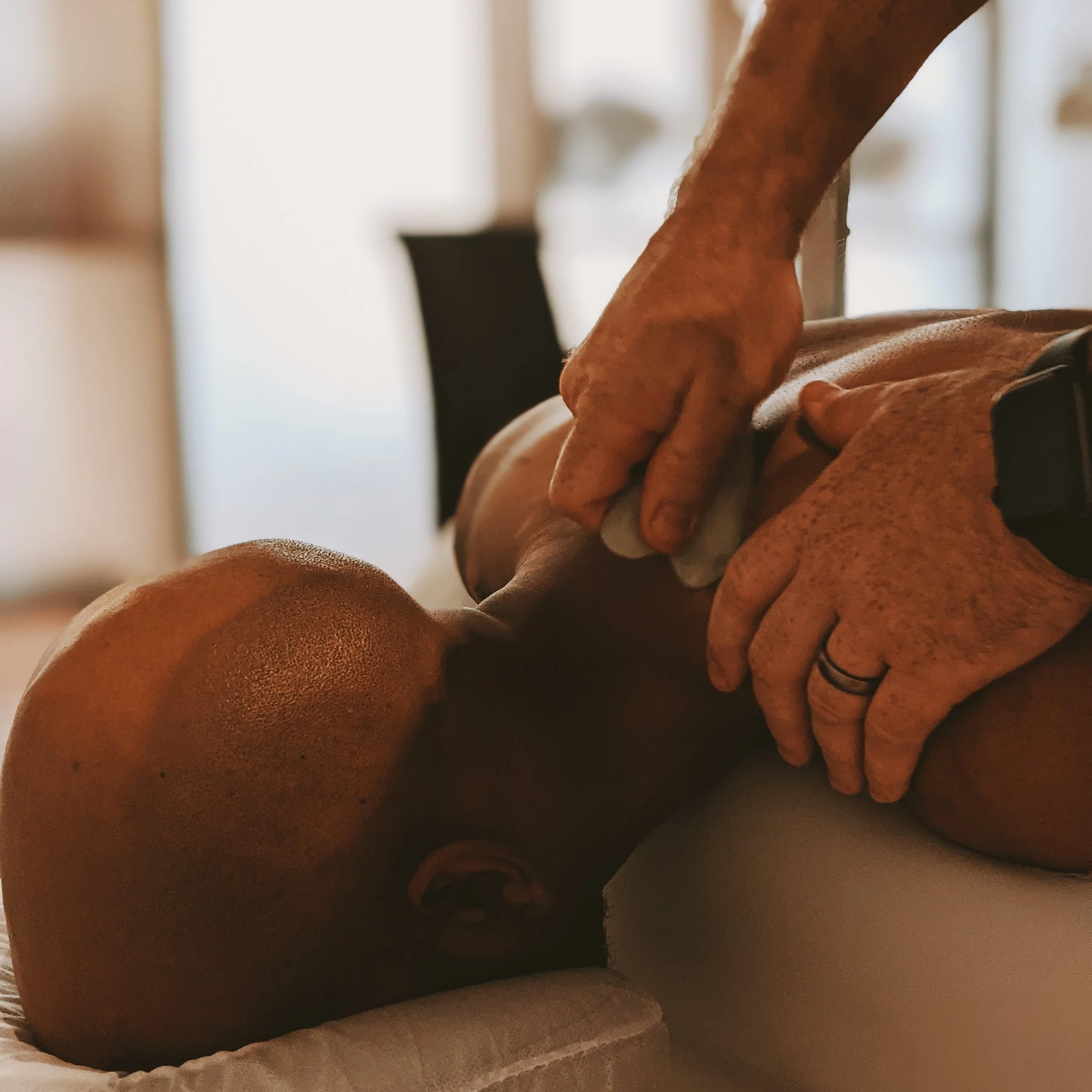 An acupuncture patient lies face down as the acupuncturist massages their neck with a gua sha tool