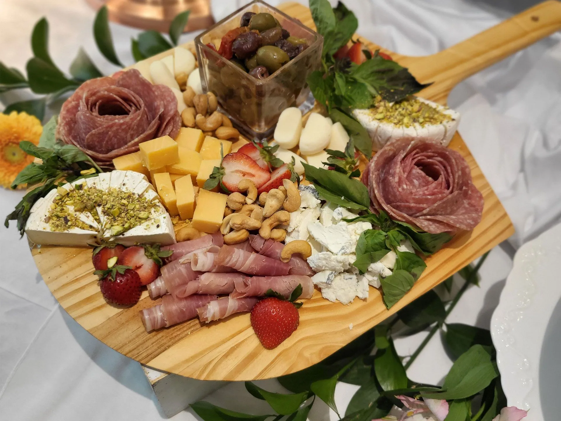 A wooden cutting board filled with meat, cheese, nuts and strawberries.