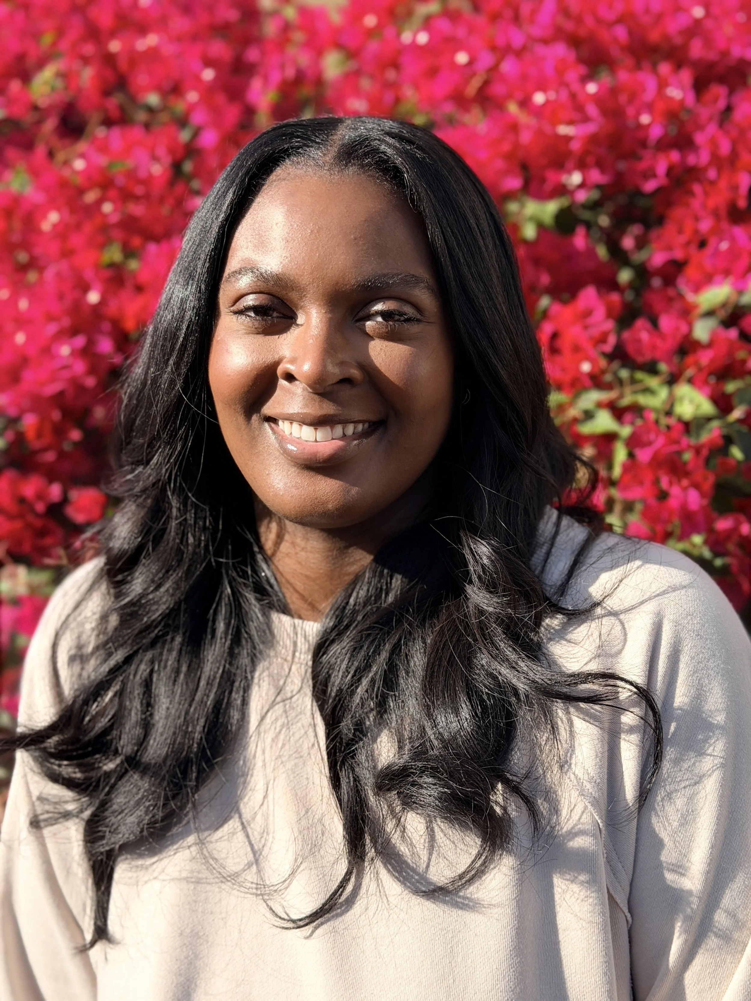 A woman smiling outdoors in front of bougainvillea flowers