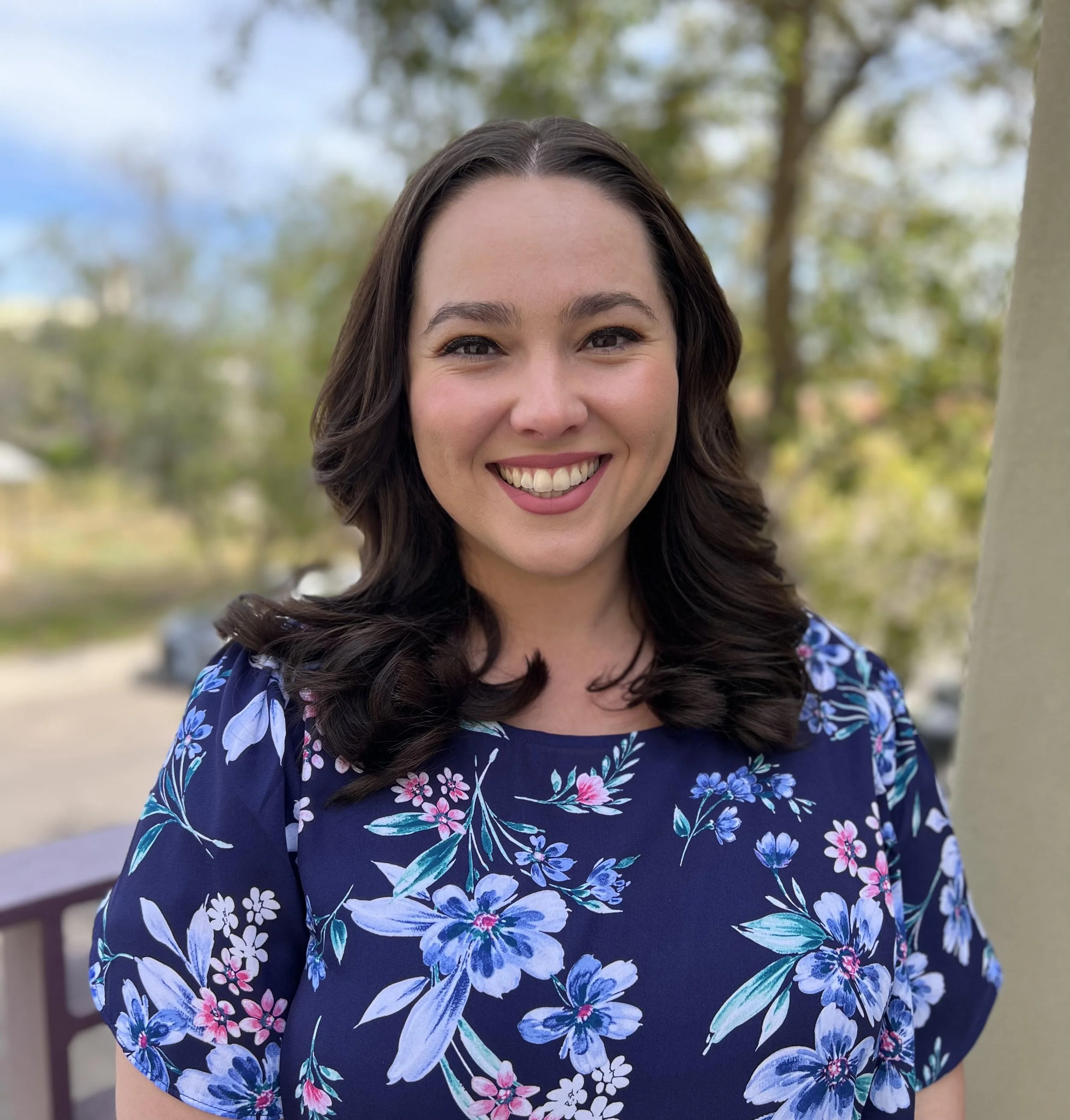 Therapist with dark brown wavy hair smiling outdoors