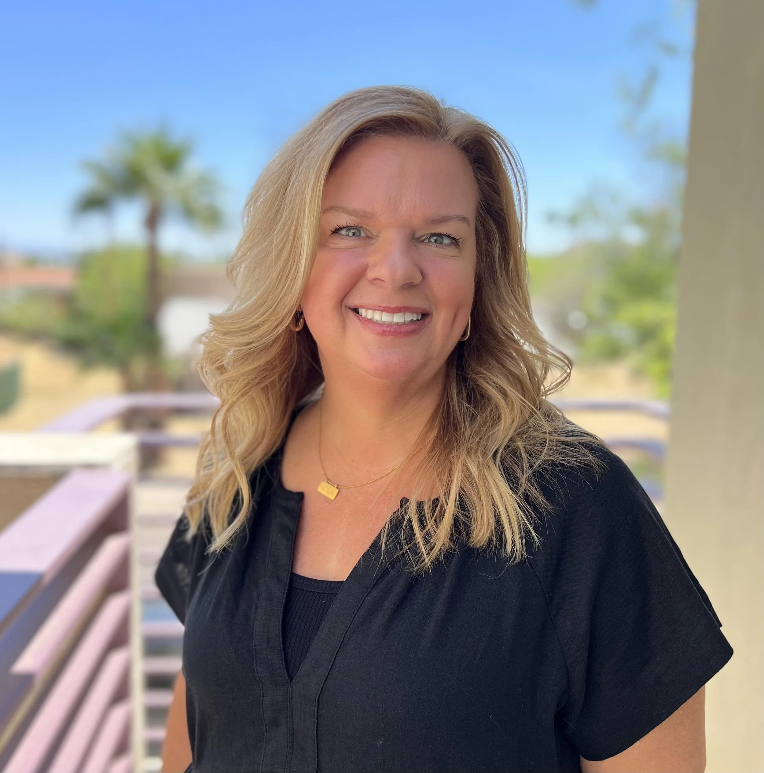 Therapist with blonde wavy hair on balcony with palm trees